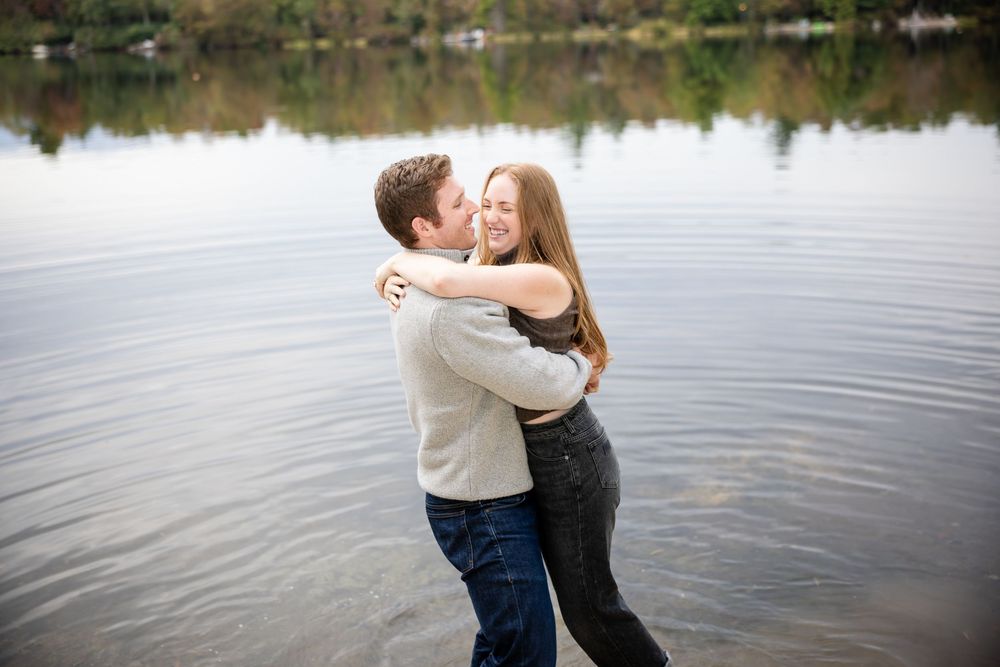 Happy couple embracing and laughing while standing in shallow lake water.