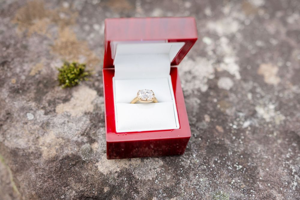 Diamond engagement ring in red jewelry box on stone surface with moss.