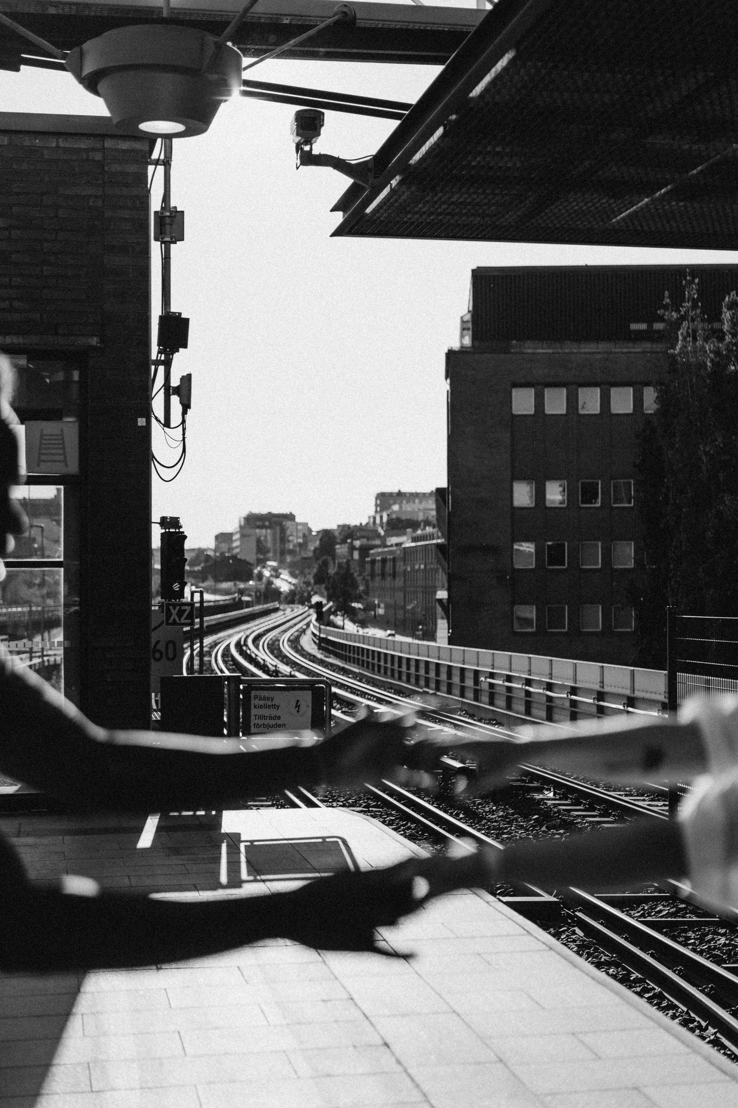 Kaksi kättä lepää vastakkain metroaseman laiturilla kaupunkiympäristössä.