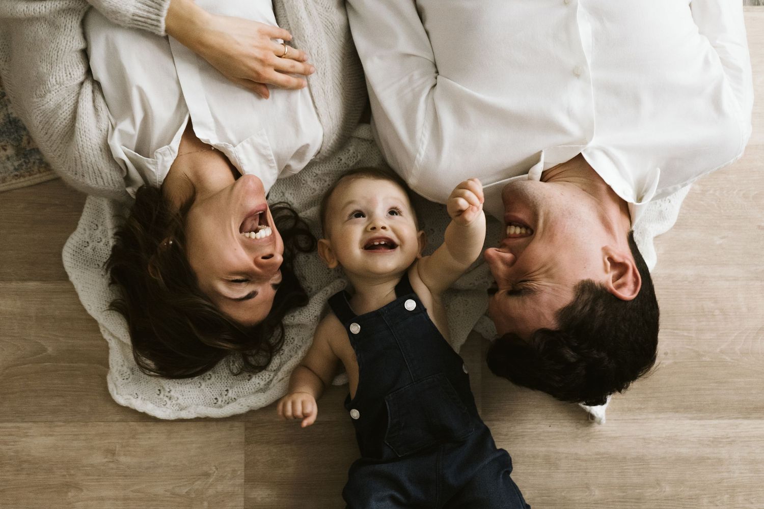 Famiglia sdraiata insieme sul pavimento di legno durante una sessione fotografica intima, divertente e spontanea.