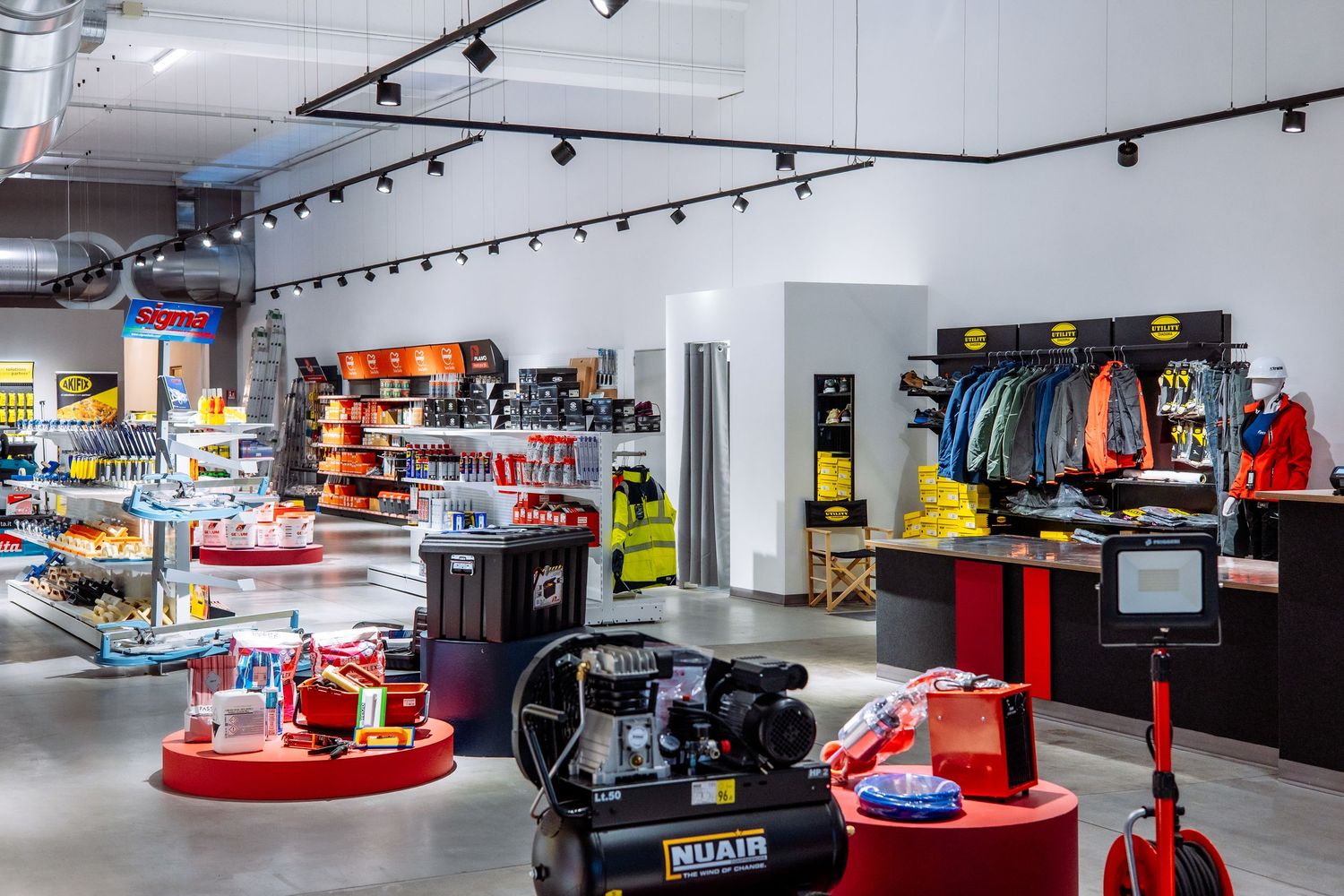 Modern retail store interior with black track lighting, red display fixtures and clothing racks along white walls.