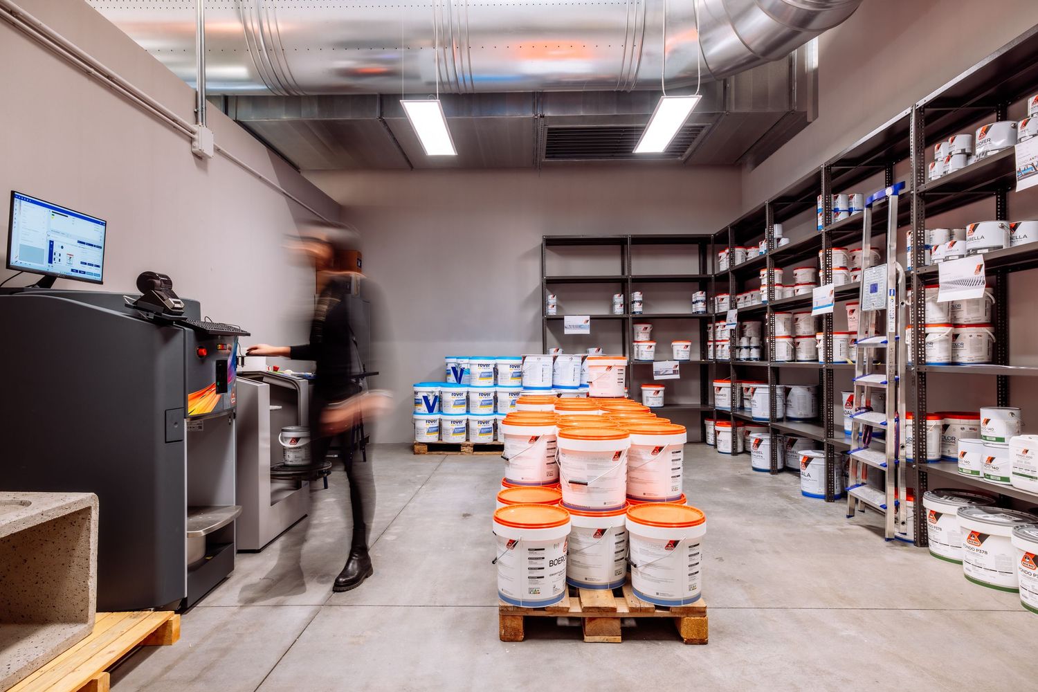 A warehouse interior with rows of industrial shelving, storage racks, and stacked pallets in a well-lit facility.