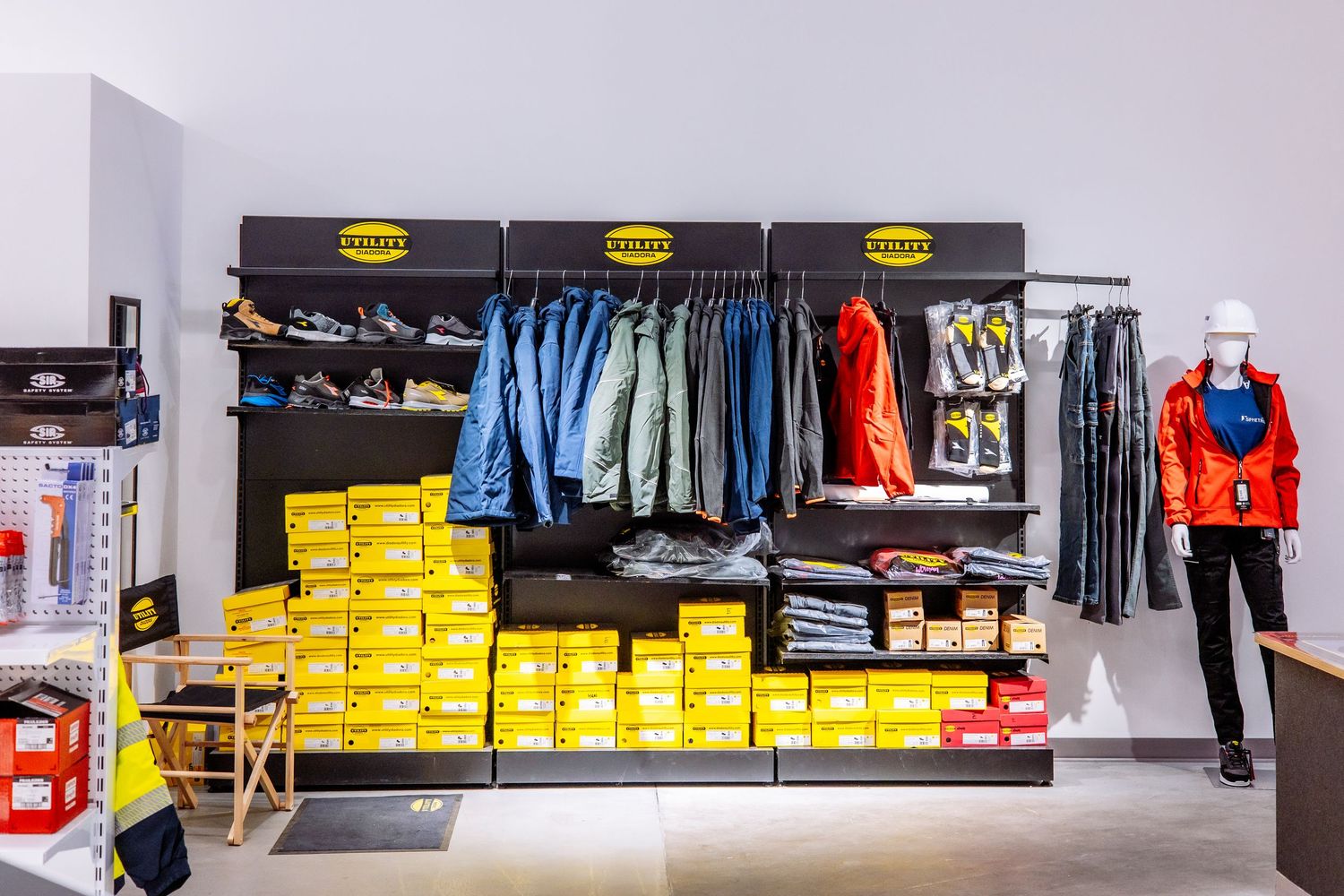 Retail clothing store display with blue jeans, yellow boxes, and red jacket on mannequin against white wall.