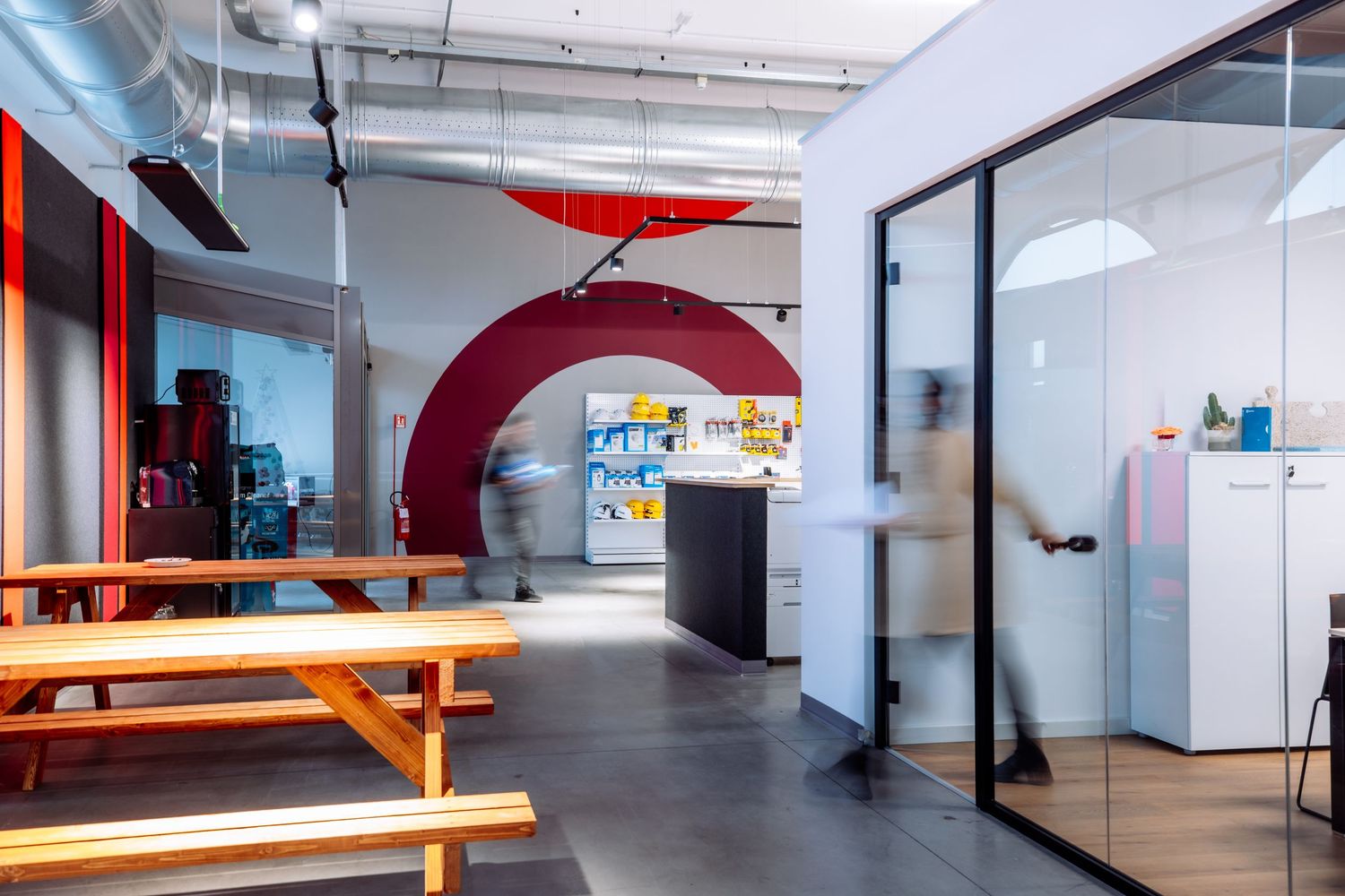 Modern office break room with red archway, wooden benches, and industrial ceiling design.