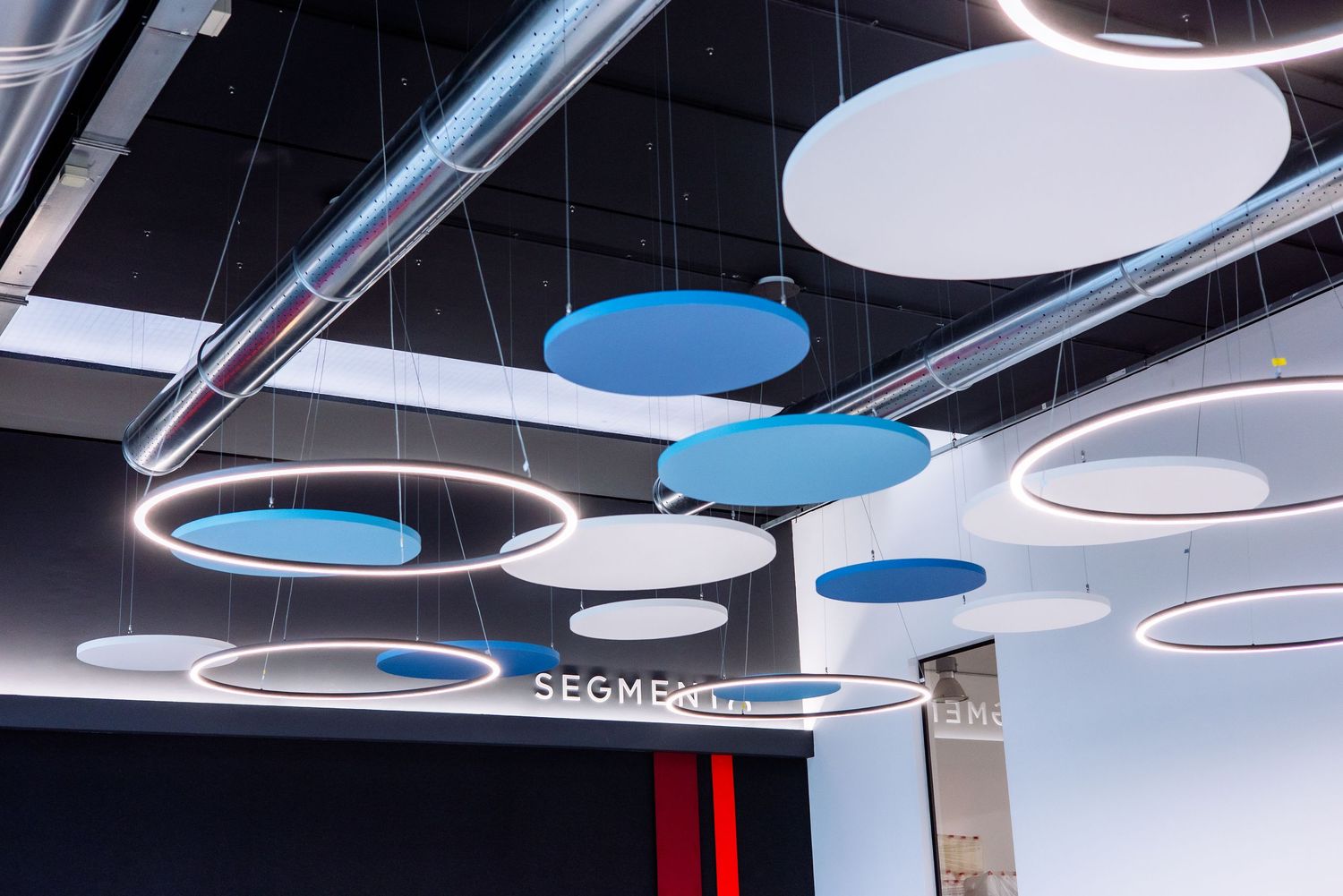 Modern office ceiling with circular pendant lights featuring blue and white illuminated panels arranged in a row.