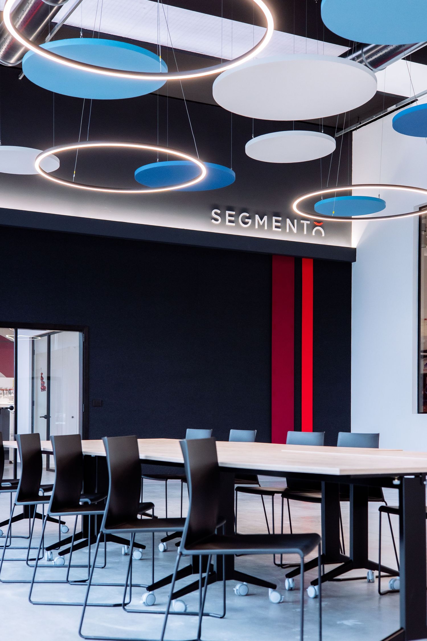Modern office interior with circular ceiling lights, blue and white decor elements, and sleek black chairs around meeting tables.