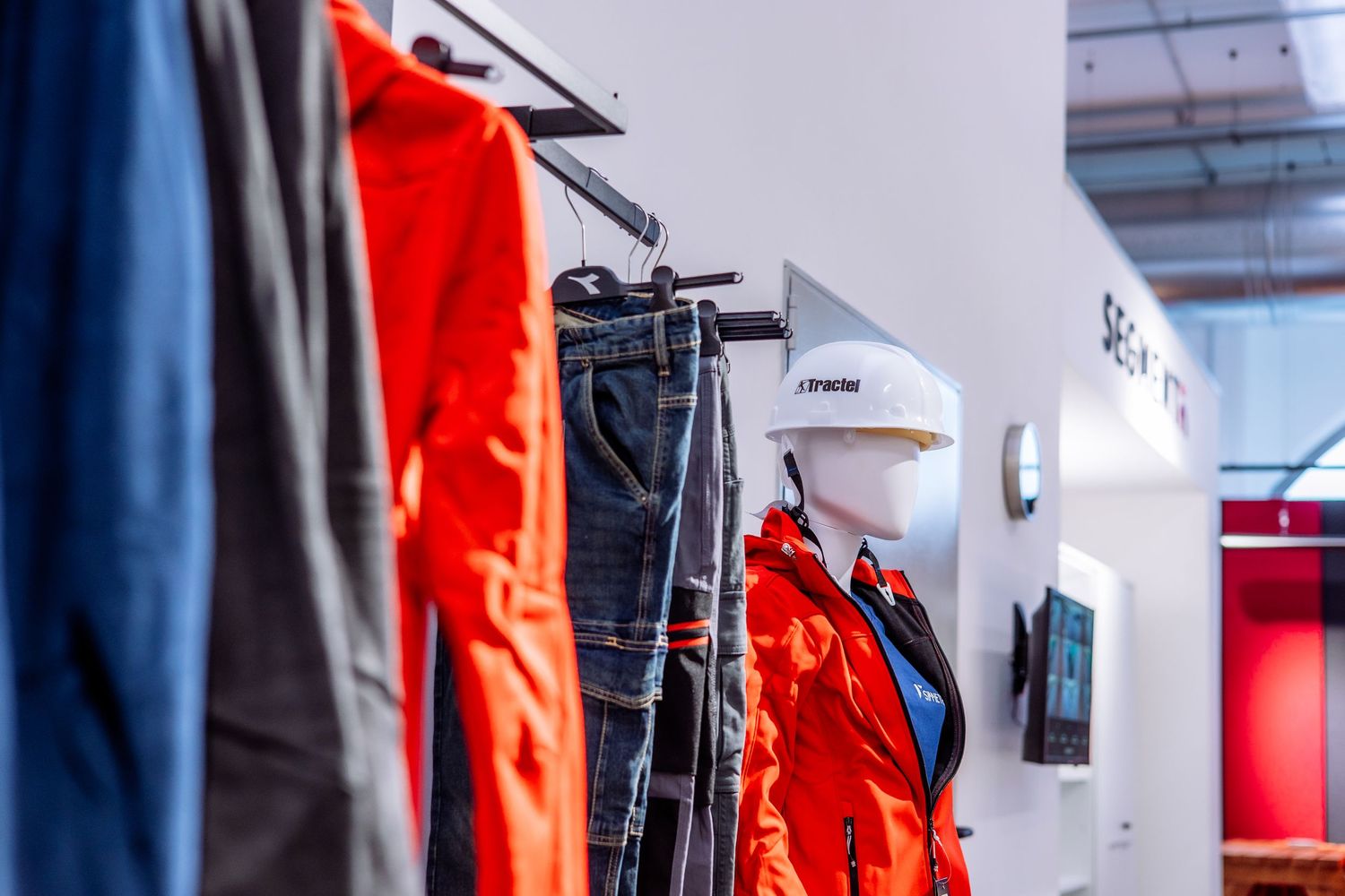 Bright orange safety vests and blue uniforms hanging on industrial storage hooks in a warehouse setting.