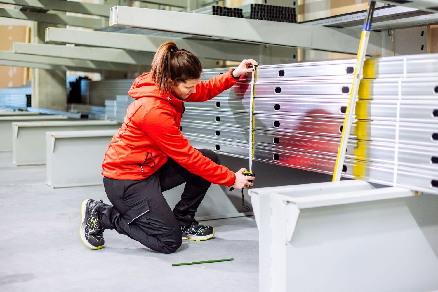 Person in red jacket and black pants installing wall shelving units in a commercial space.