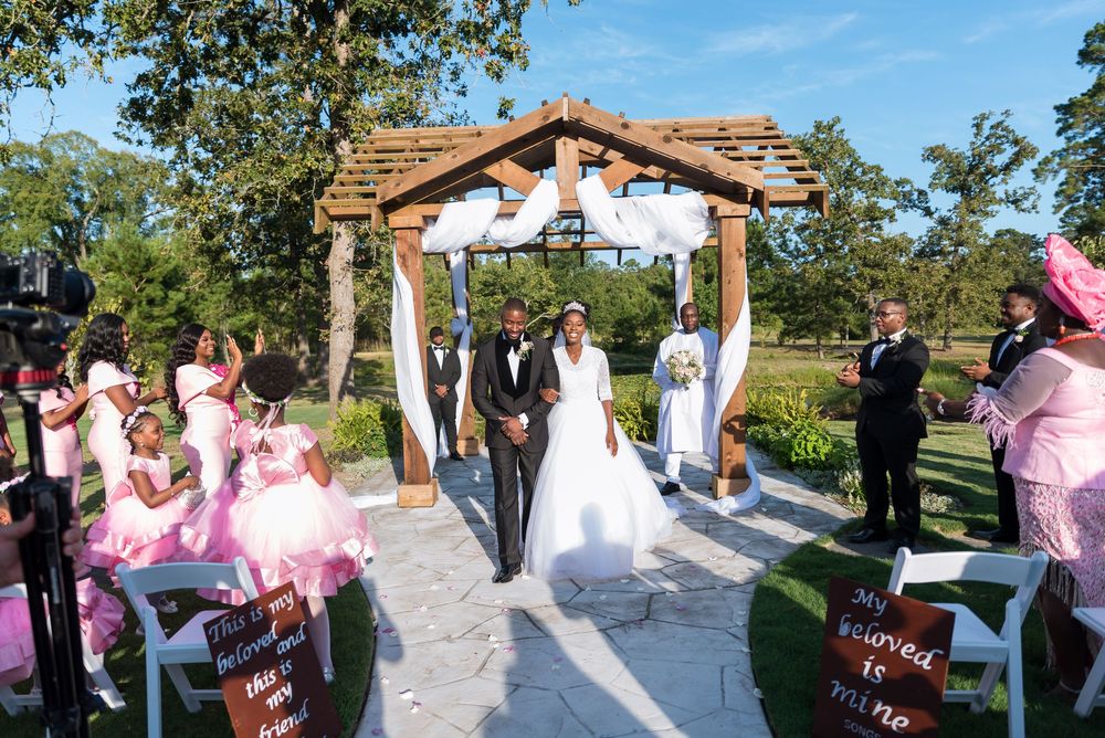 Wedding ceremony guests gather outside a rustic wooden venue surrounded by trees on a sunny day. Couple wedding ceremony in Houston