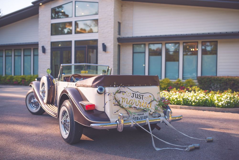 Vintage white wedding car with 'Just Married' sign parked outside a modern building with tinted windows.