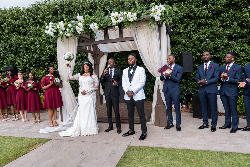 Wedding party stands in line on garden steps wearing burgundy dresses and navy suits during outdoor ceremony.