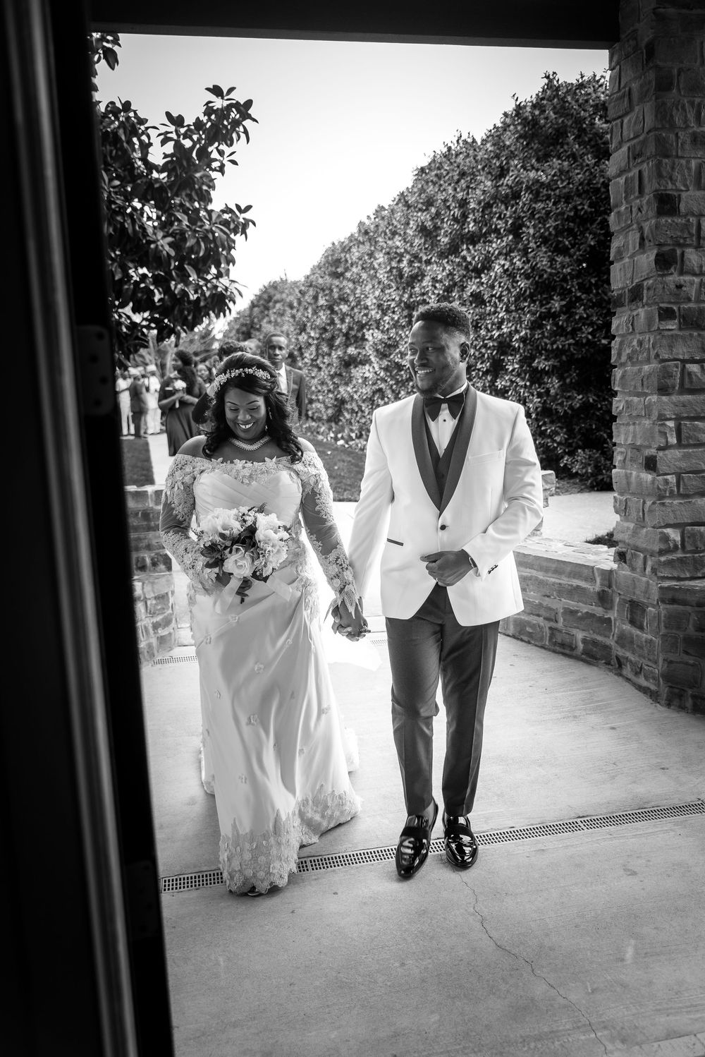 Black and white wedding photograph showing a couple walking down a stone-lined outdoor pathway together.
