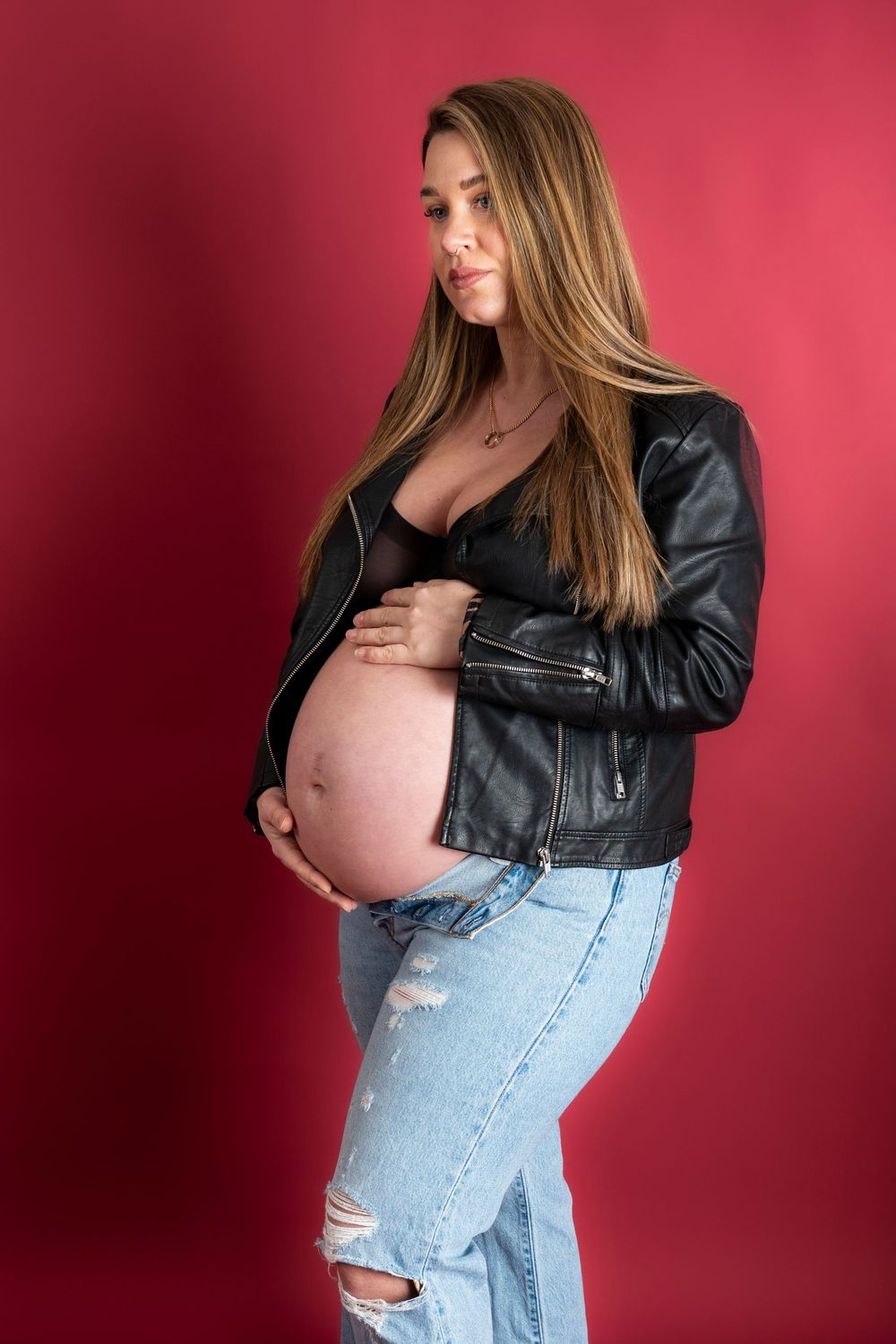 Maternity photo series showing a pregnant woman in ripped jeans and leather jacket against a pink background.