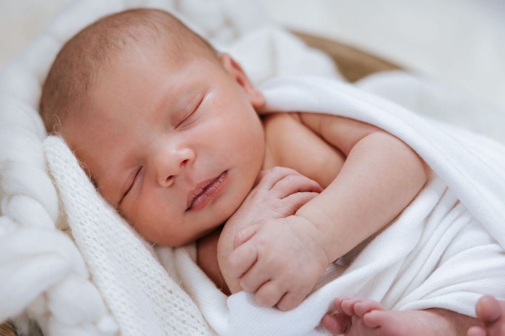 Serene newborn swaddled in soft white fabric sleeping peacefully against light backdrop.