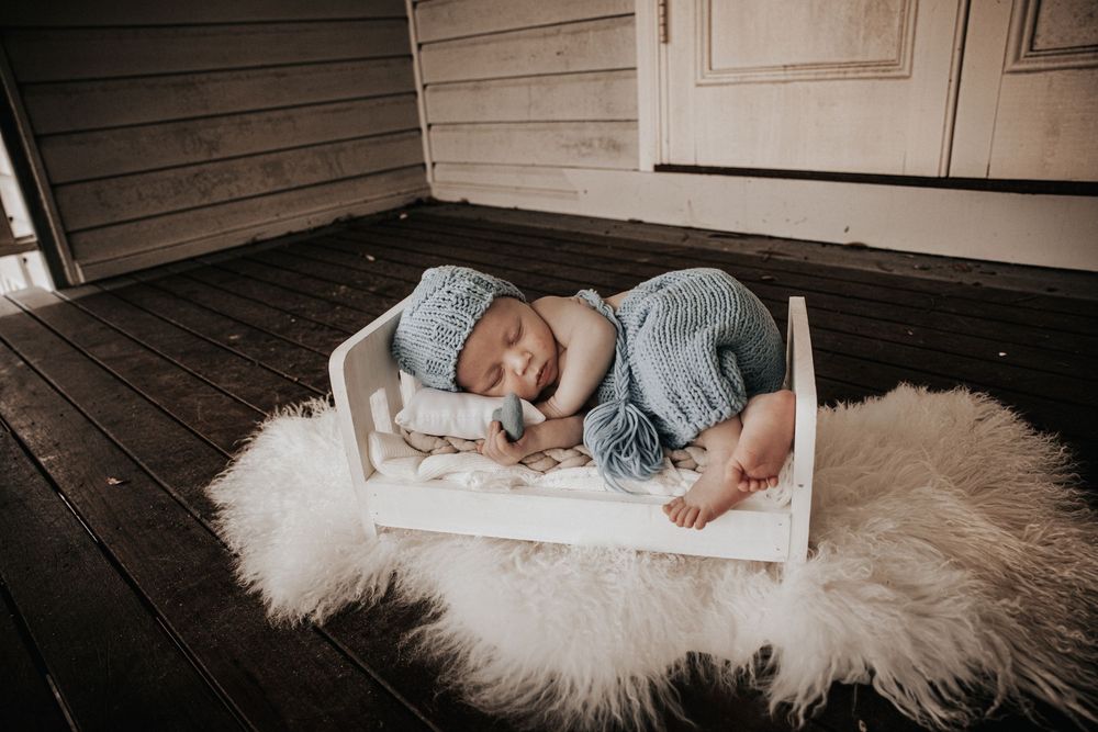 A series of dreamy newborn photos featuring a sleeping baby in white boxes on a fluffy white rug.