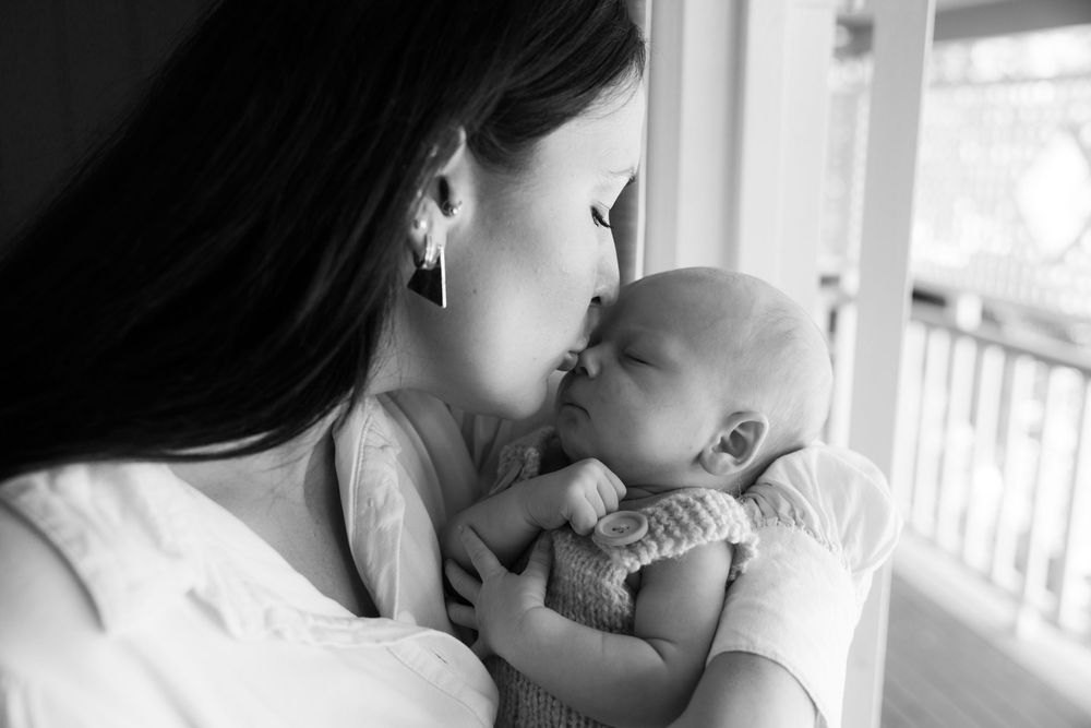 A series of intimate black and white photos showing tender moments between a parent and baby in window light.