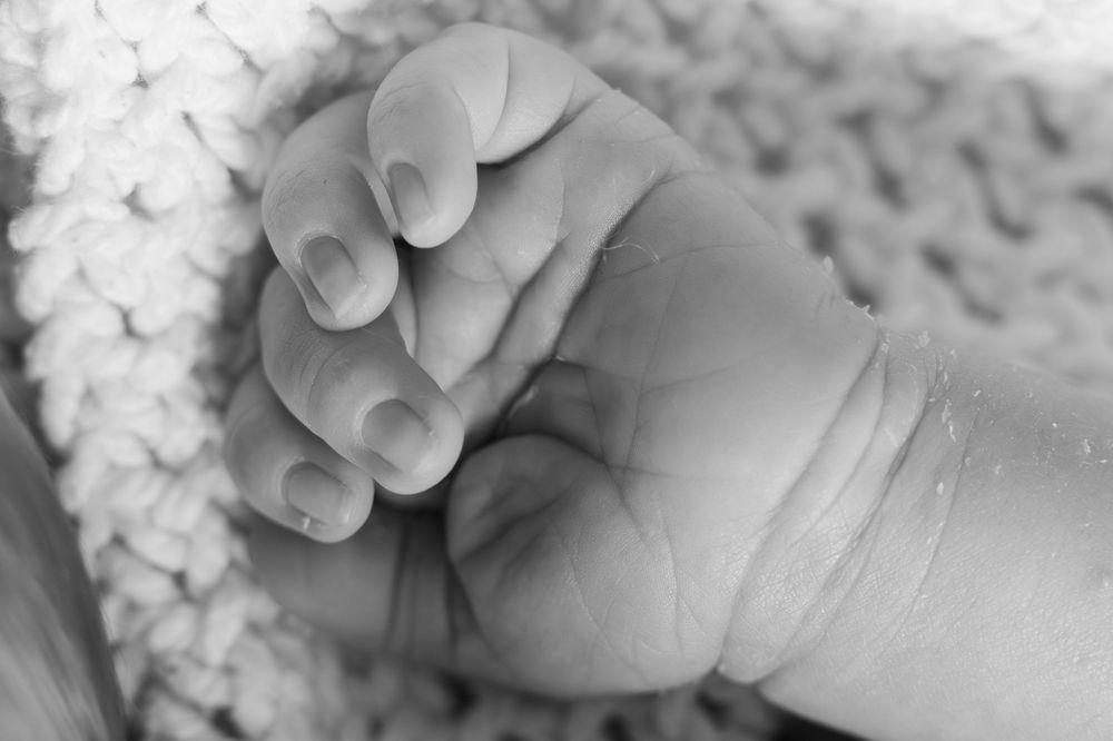 A close-up black and white photograph shows a baby's tiny hand grasping an adult's finger.