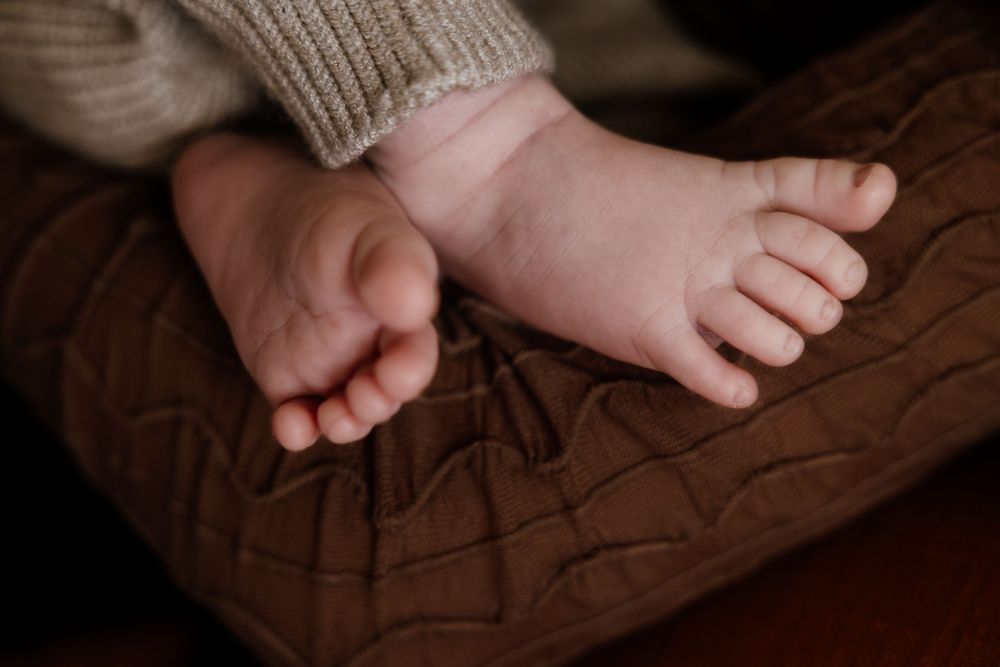 Small bare baby feet resting on brown leather furniture in a dimly lit room.