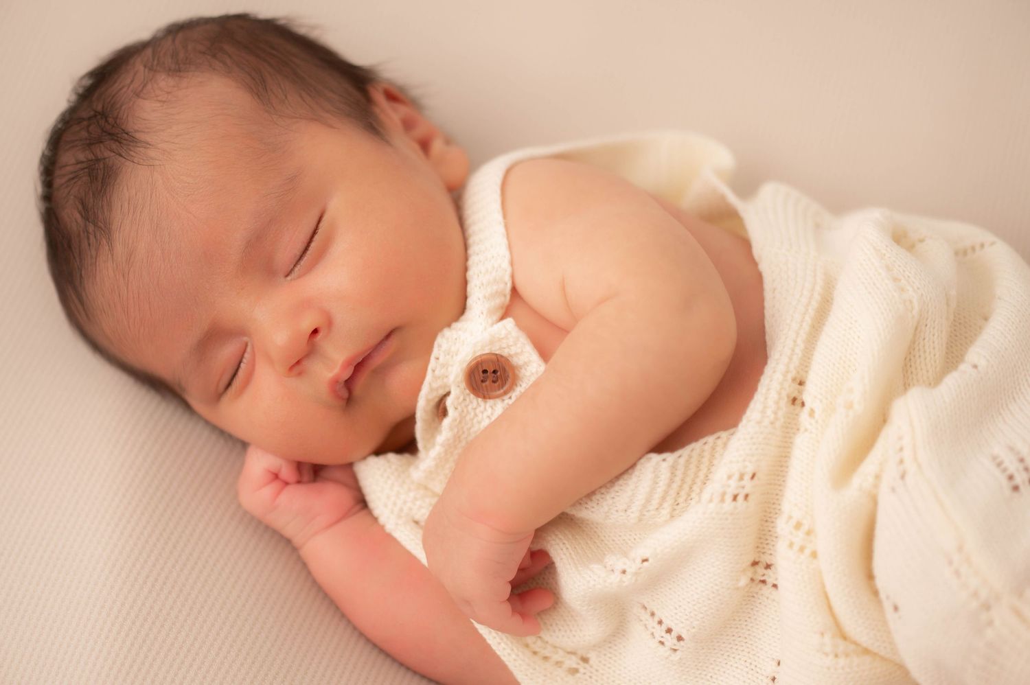 A sleeping newborn baby wearing white angel wings and a headband.