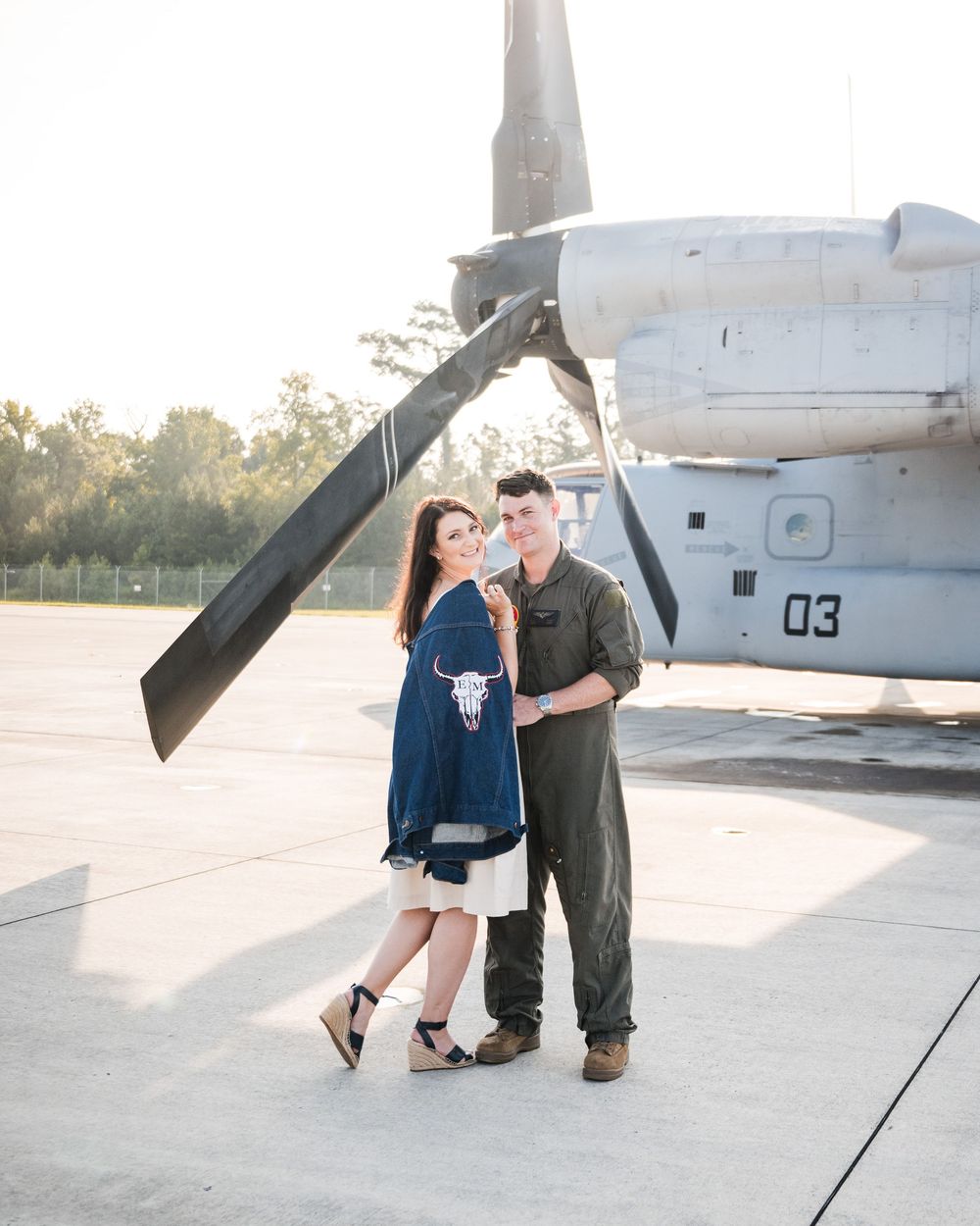 Military couple shares romantic moments near an aircraft on a sunny airfield.