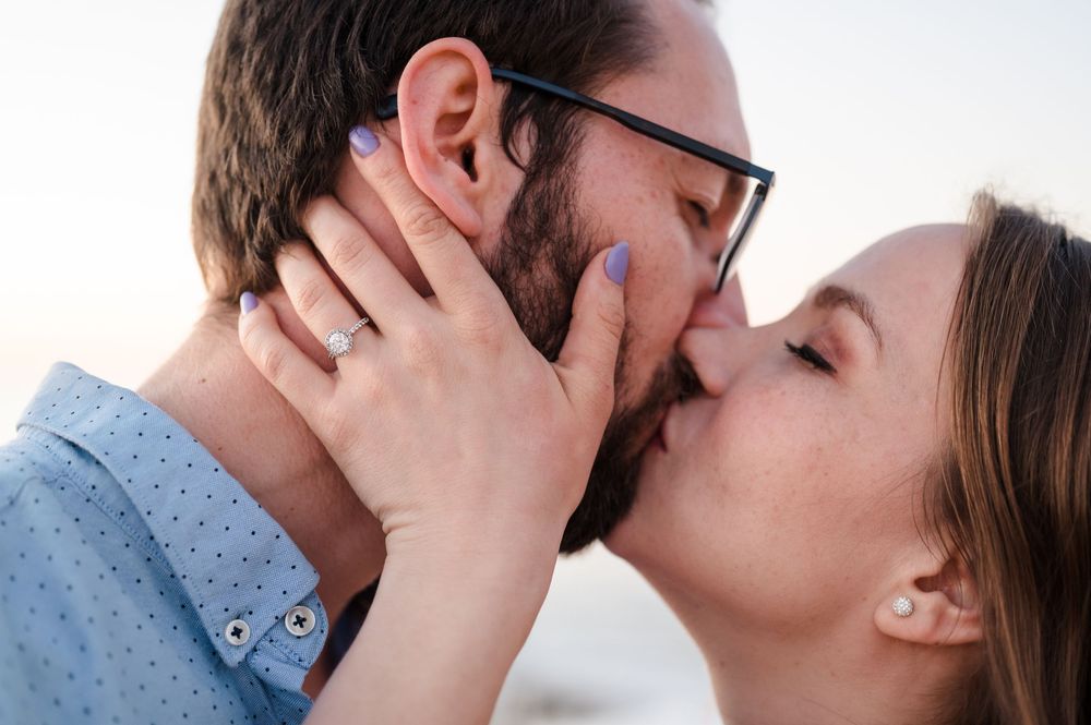A couple shares a romantic kiss against a bright white background.