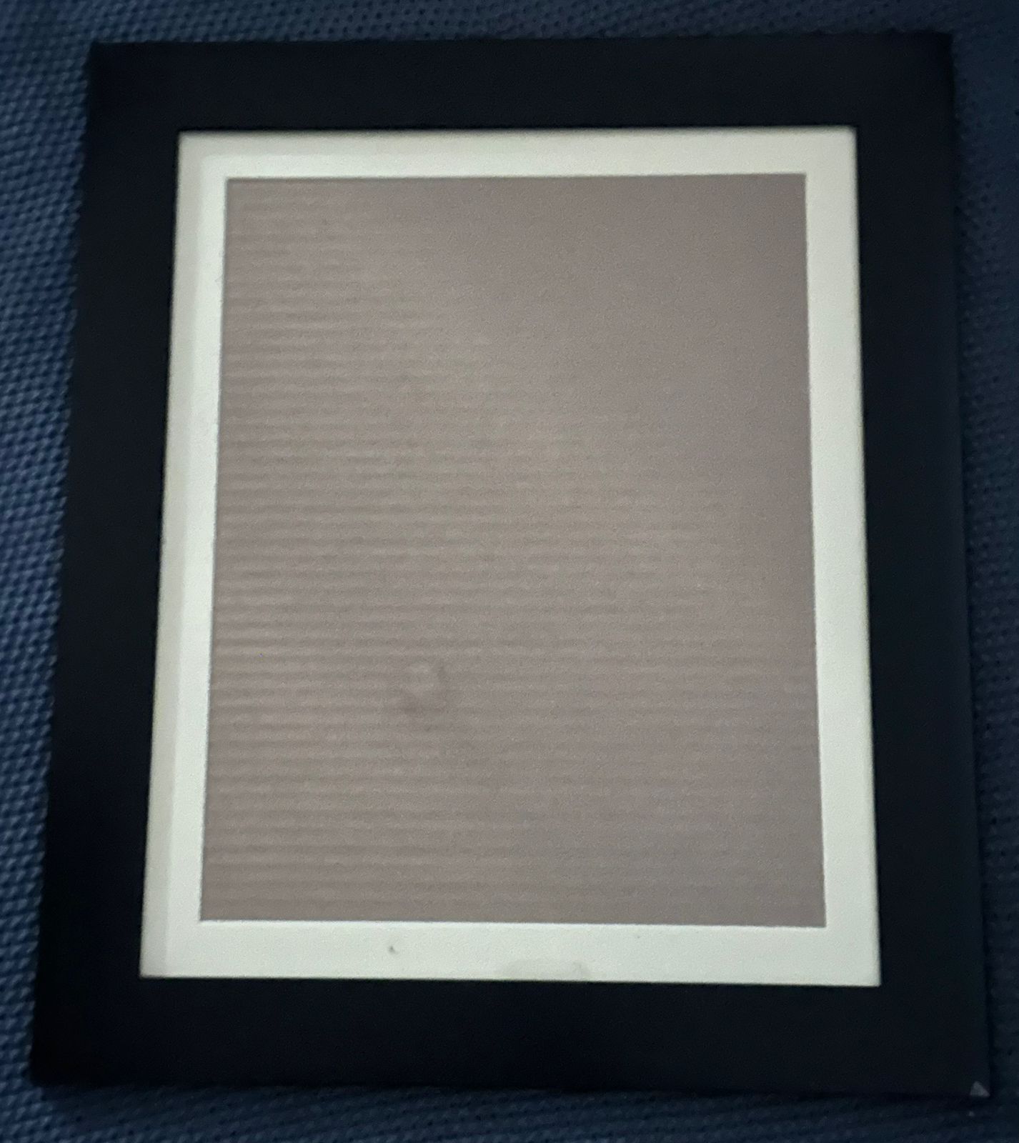 Empty black picture frame with white matting and tan colored center displayed against dark textured background.