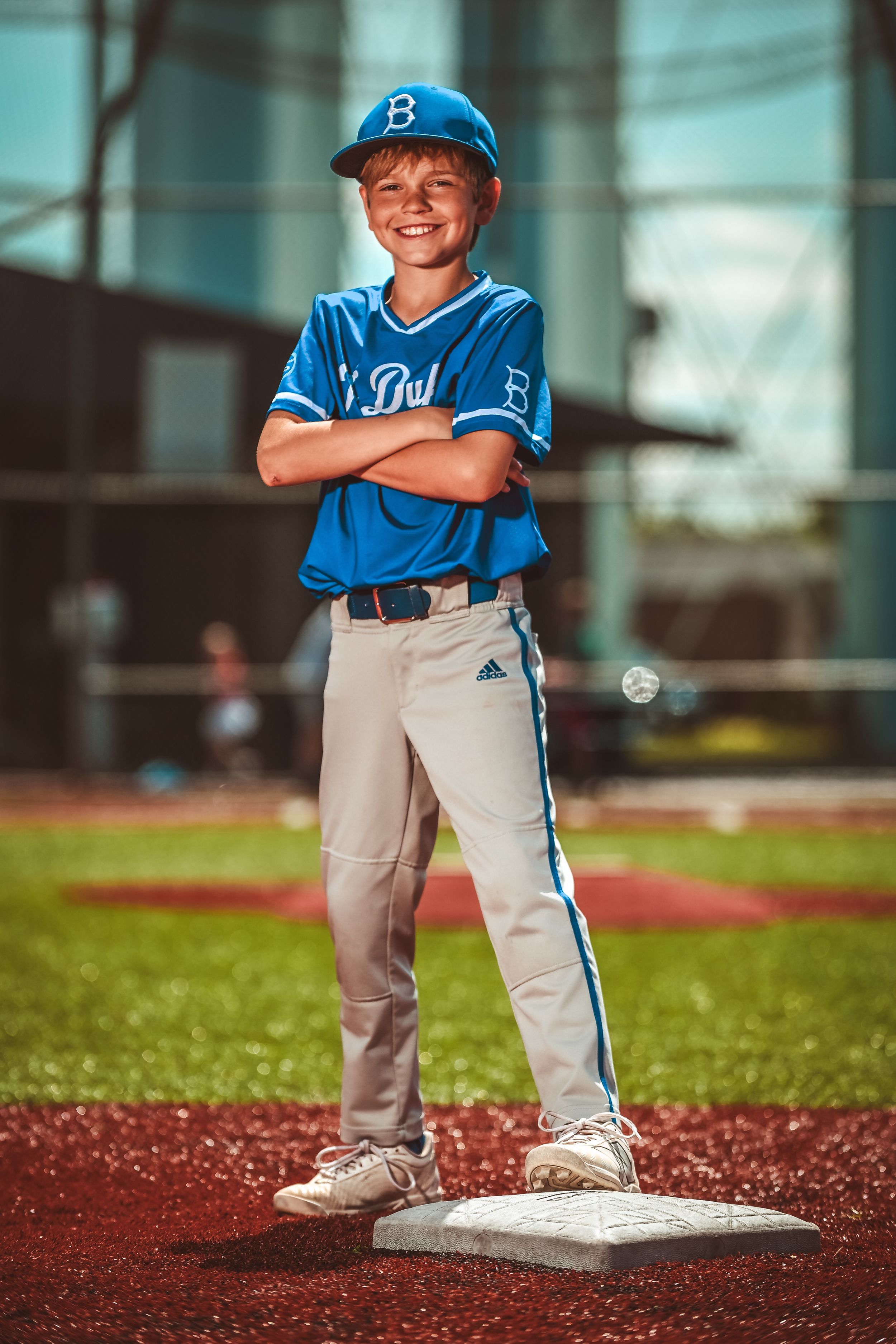 Young baseball player in blue uniform standing on base during a game on red turf field.