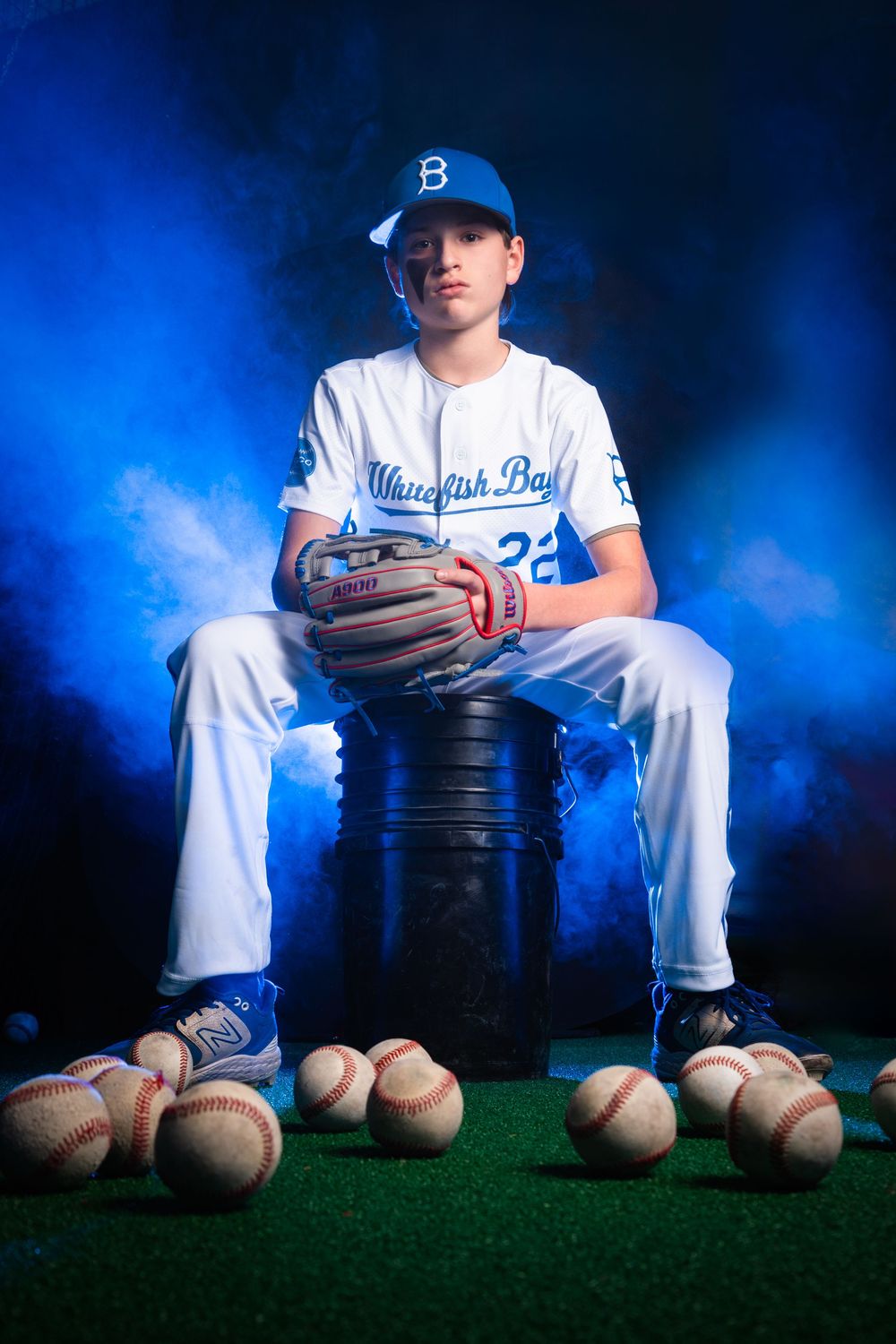Baseball player in Dodgers uniform sits with baseballs and equipment against dramatic blue background.