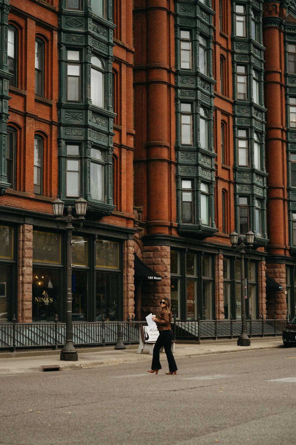 Historic brownstone buildings with ornate architecture line a city street as people walk past on a cloudy day.
