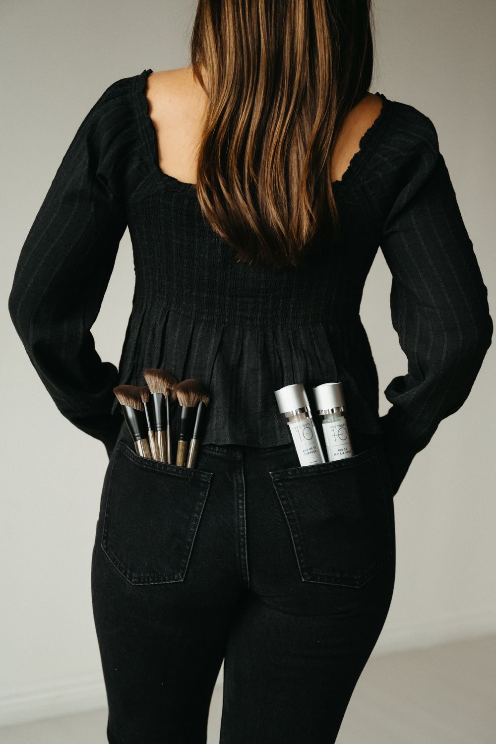 Person wearing all black outfit showing makeup brushes in back pockets.