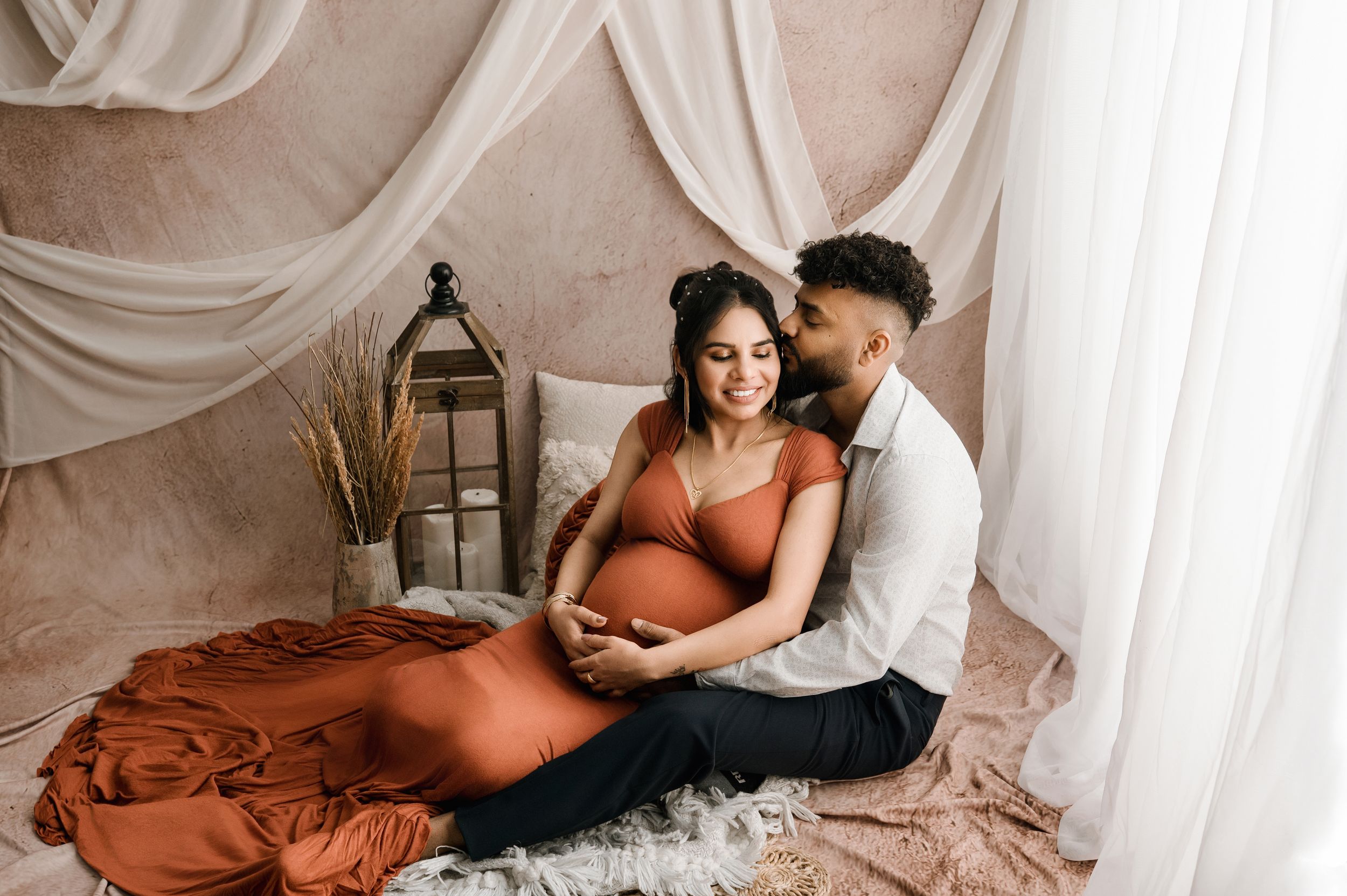 A series of intimate maternity photos showing a couple in a light-filled bedroom with white curtains and terracotta bedding.