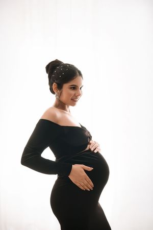 Elegant maternity portrait of a woman in a black off-shoulder dress against a white background.