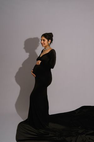 A figure in a flowing black dress poses dramatically against a light backdrop with strong shadow effects.