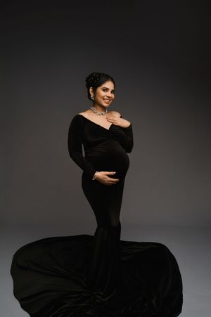 Elegant maternity photo featuring a woman in a flowing black velvet gown against a dark gray backdrop.