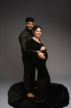 Elegant maternity photo featuring a couple in matching black outfits embracing against dark background.