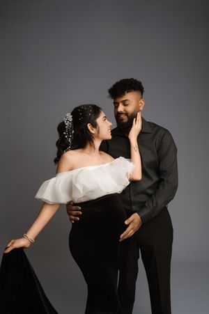 A romantic couple embraces in formal attire against a gray backdrop during an elegant photoshoot.