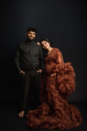 A fashion photoshoot featuring a dramatic flowing rust-colored gown against a dark background.