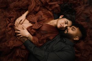 A person lies on a bed of autumn leaves wearing dark clothing and burgundy accessories in an artistic composition.