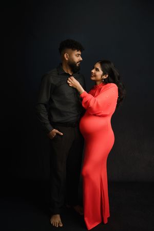 A couple in a romantic pose against a dark background, with the woman wearing a vibrant red dress.