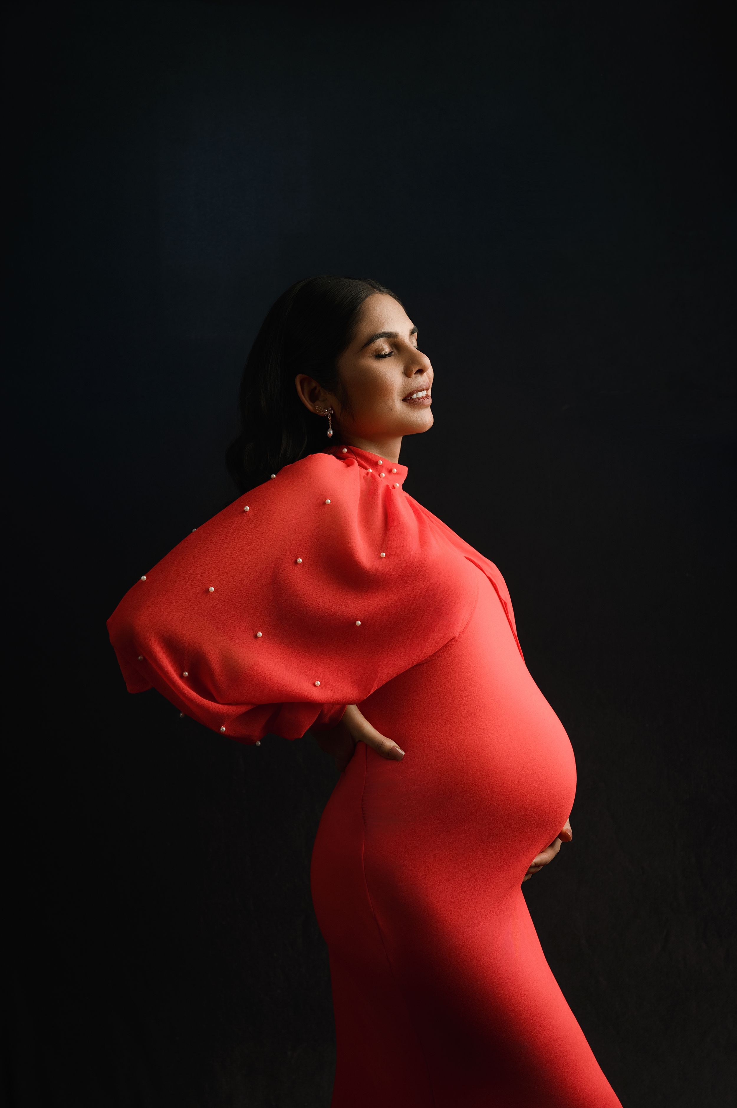 Dramatic silhouette of a pregnant woman in a red dress posing against a dark background with glittering light effects.