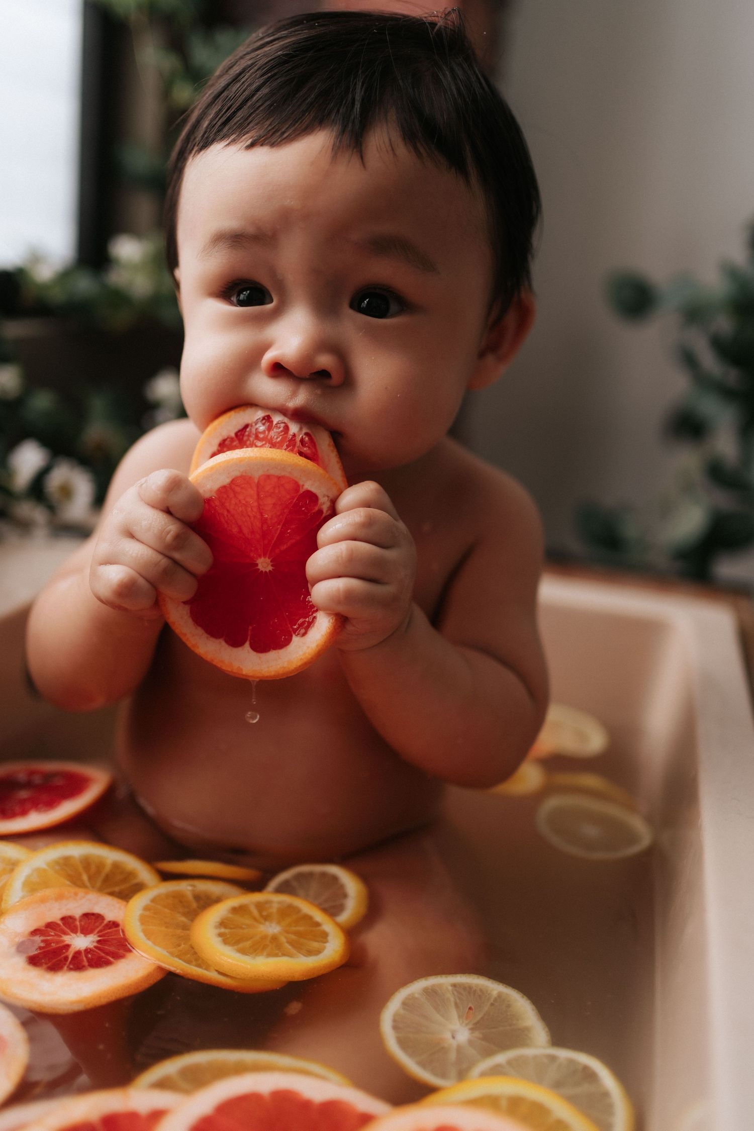 Small child enjoying a citrus fruit bath with sliced oranges, lemons and grapefruits arranged in water.
