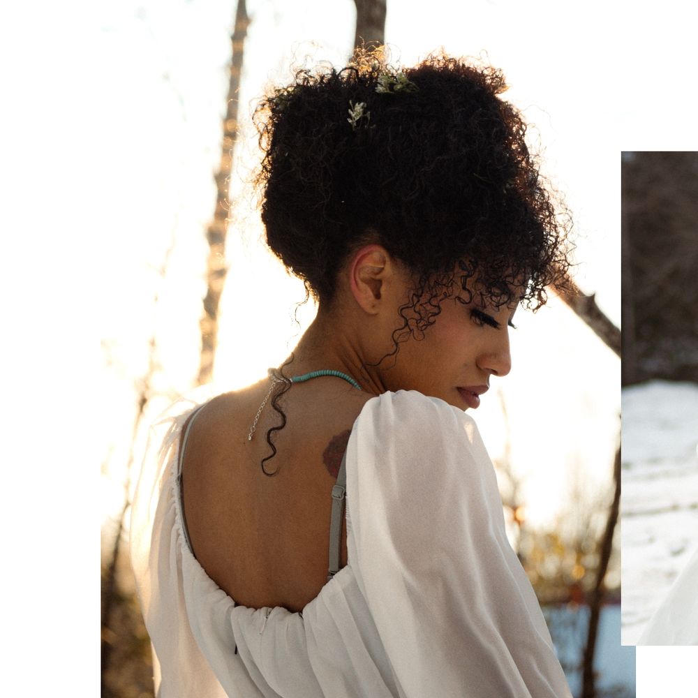 Person with curly hair in white clothing photographed from behind at sunset.