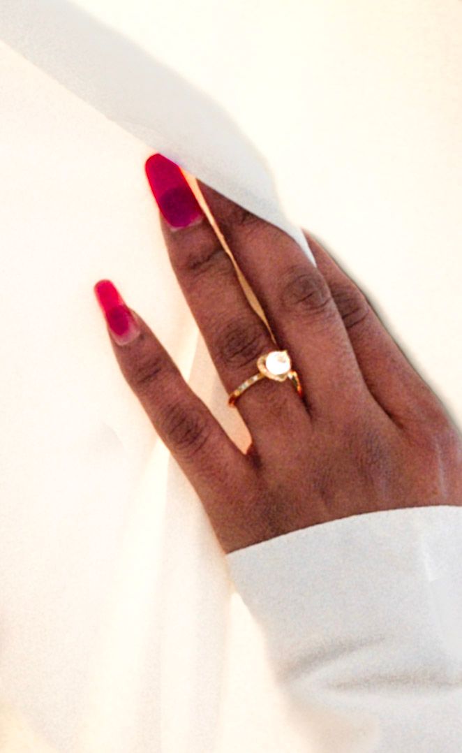 Hand with red manicure and engagement ring against white background.