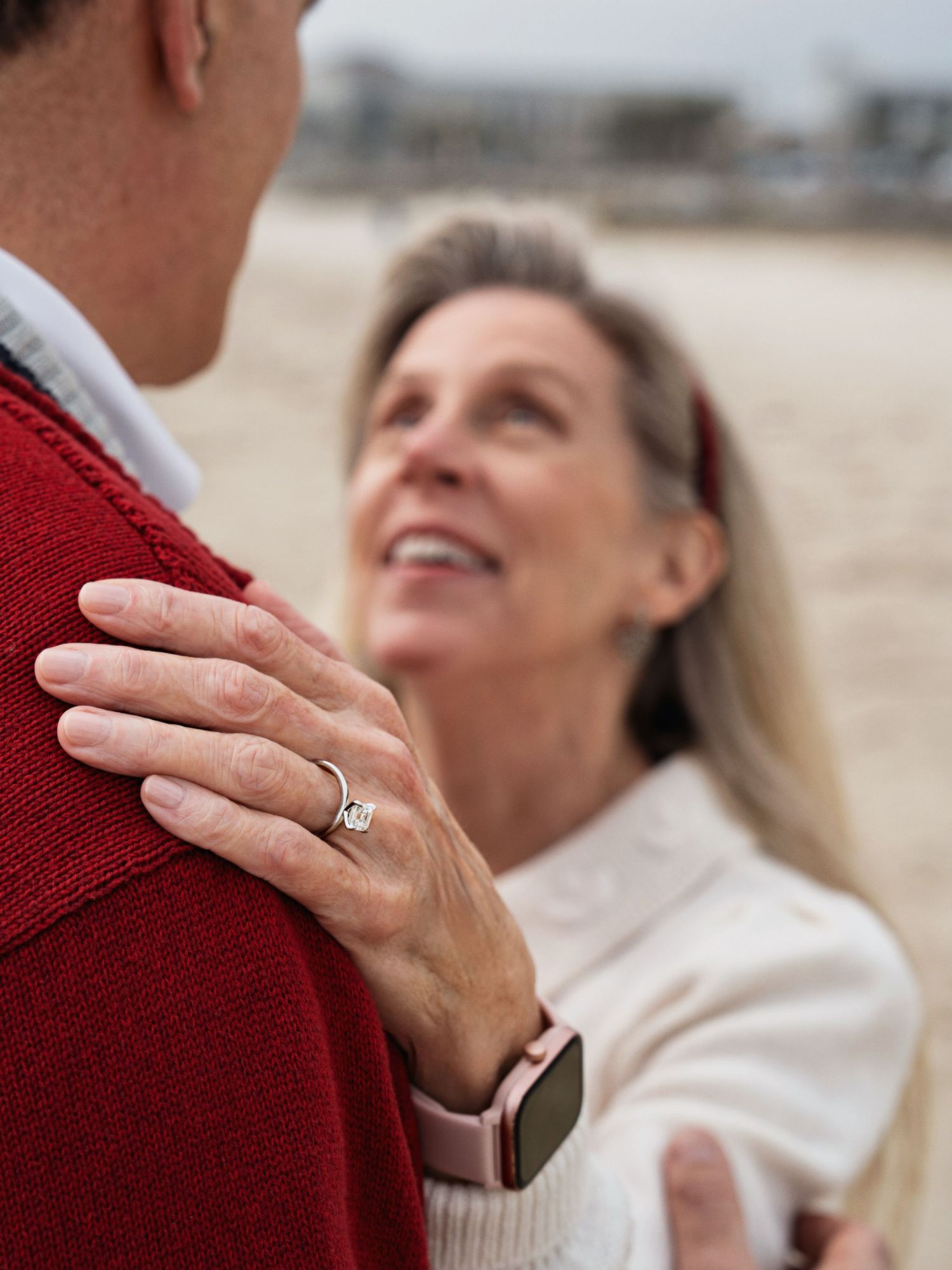 Close up of hands and ring on red sweater against beach background.