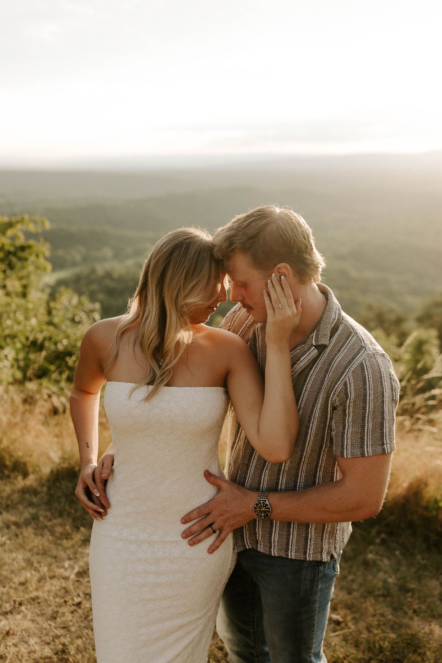 Blonde woman in pink sundress walking through sunlit green field at golden hour.
