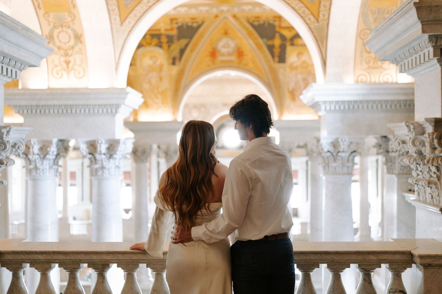 Couple shares romantic moment on ornate staircase in elegant venue with mural backdrop.