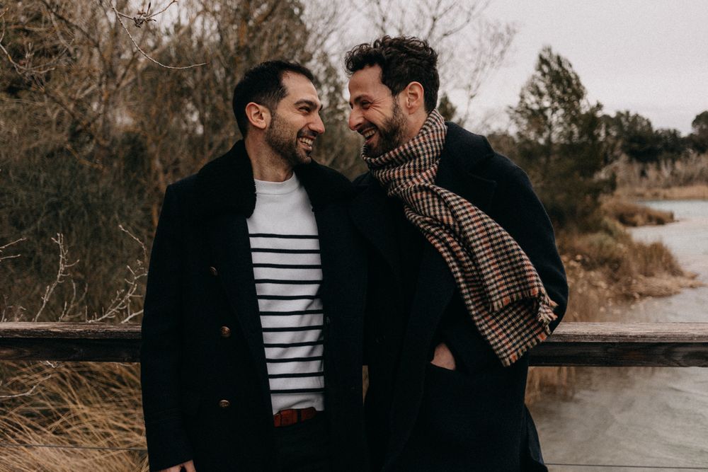 A couple wearing black coats and striped shirts embrace outdoors on a winter day.