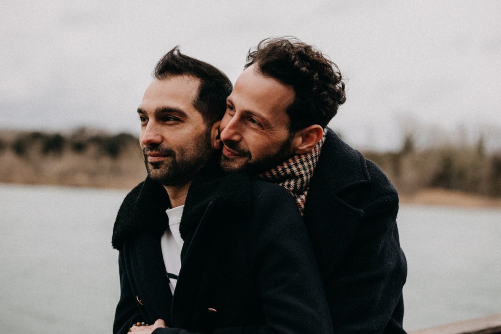 A joyful couple sharing a candid moment together by a waterfront on an overcast day.