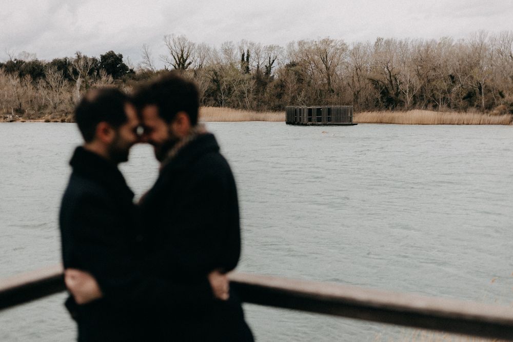 Two silhouettes embrace on a wooden dock overlooking a serene lake with winter trees in the background.