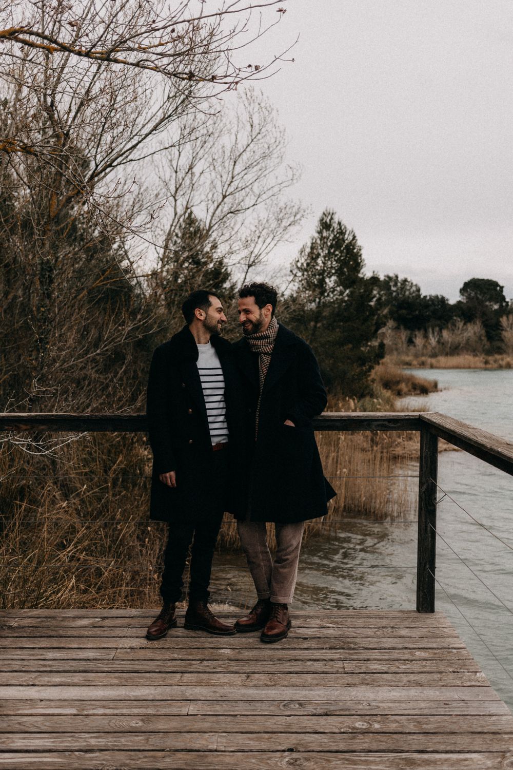 A couple shares an intimate moment on a wooden boardwalk overlooking a serene lake during winter.